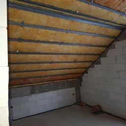 Paweł Lisowicz Usługi Ogólnobudowlane - Skośne poddasze z widoczną izolacją z wełny mineralnej między metalowymi profilami, ściany z białych bloczków. Etap prac przed wykończeniem.