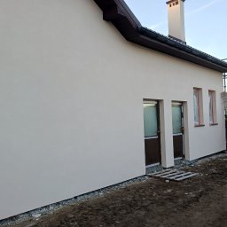 Paweł Lisowicz Usługi Ogólnobudowlane - Jasna elewacja domu jednorodzinnego po tynkowaniu, z widocznymi oknami zabezpieczonymi folią i drabiną opartą o ścianę. Świeżo wykończona ściana w neutralnym odcieniu.