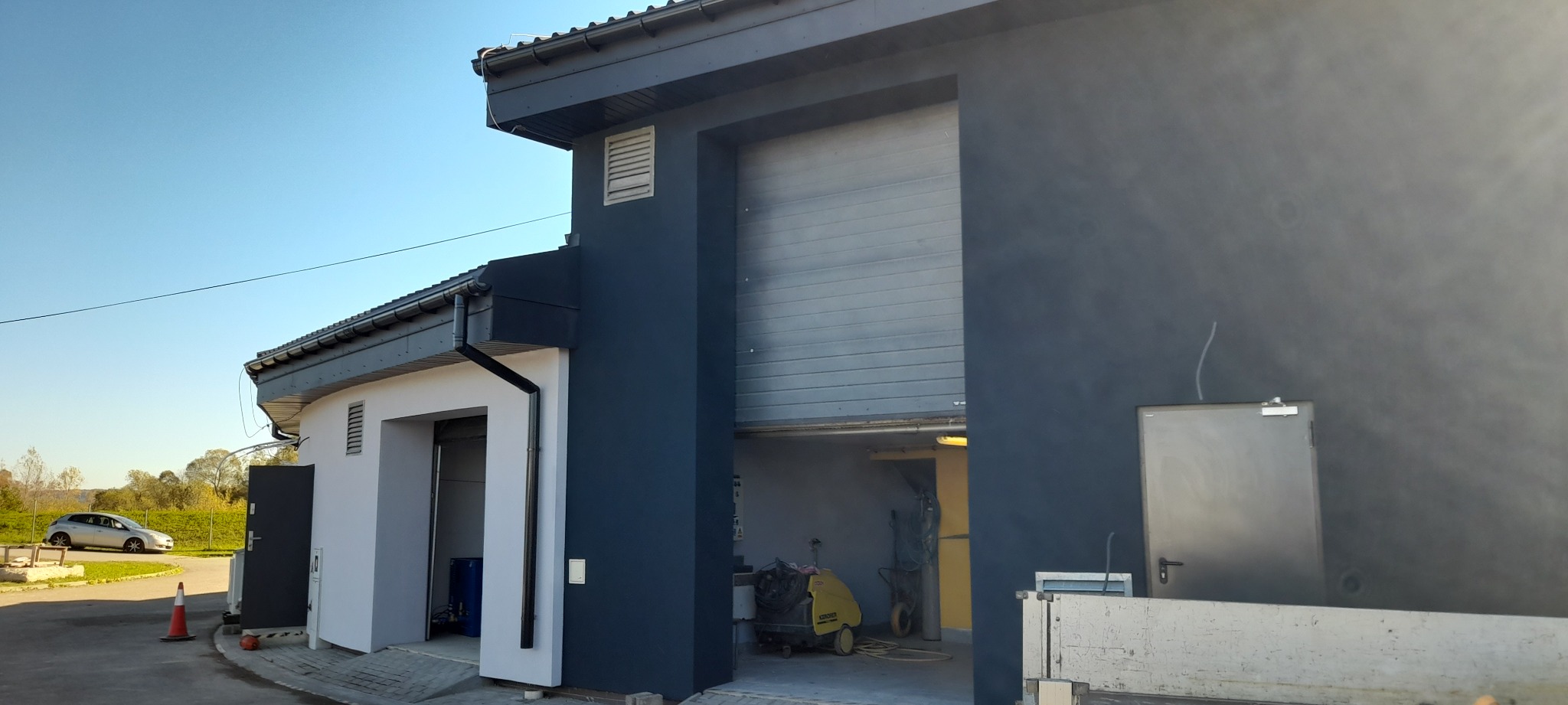 Budynek po renowacji z otwartymi bramami garażowymi, pomalowany na szaro, z widocznym samochodem w tle i sprzętem wewnątrz garażu.