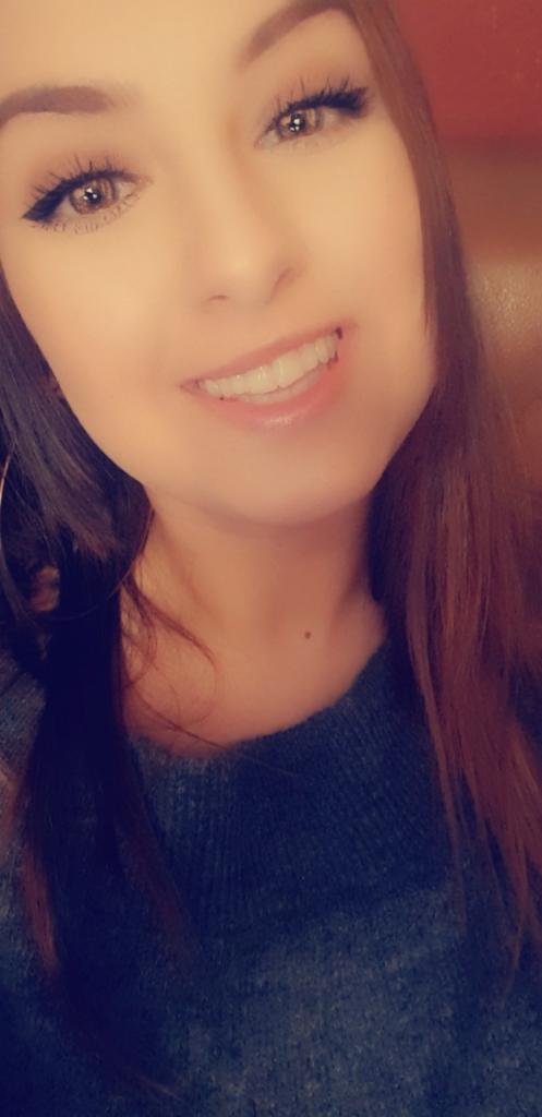 Portret uśmiechniętej kobiety z długimi, rudymi włosami i makijażem oczu, prezentującej białe zęby.