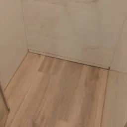 Wykończona kabina prysznicowa z panelami imitującymi drewno na podłodze i białymi płytkami imitującymi marmur na ścianach, widoczny srebrny wąż prysznicowy.