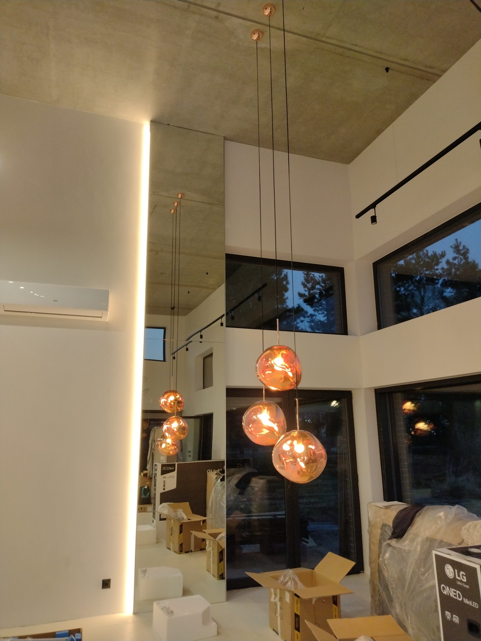 Nowoczesne, szklane lampy wiszące z miedzianymi akcentami w przestronnym wnętrzu we Wrocławiu, z widocznym betonowym sufitem i dużymi oknami.