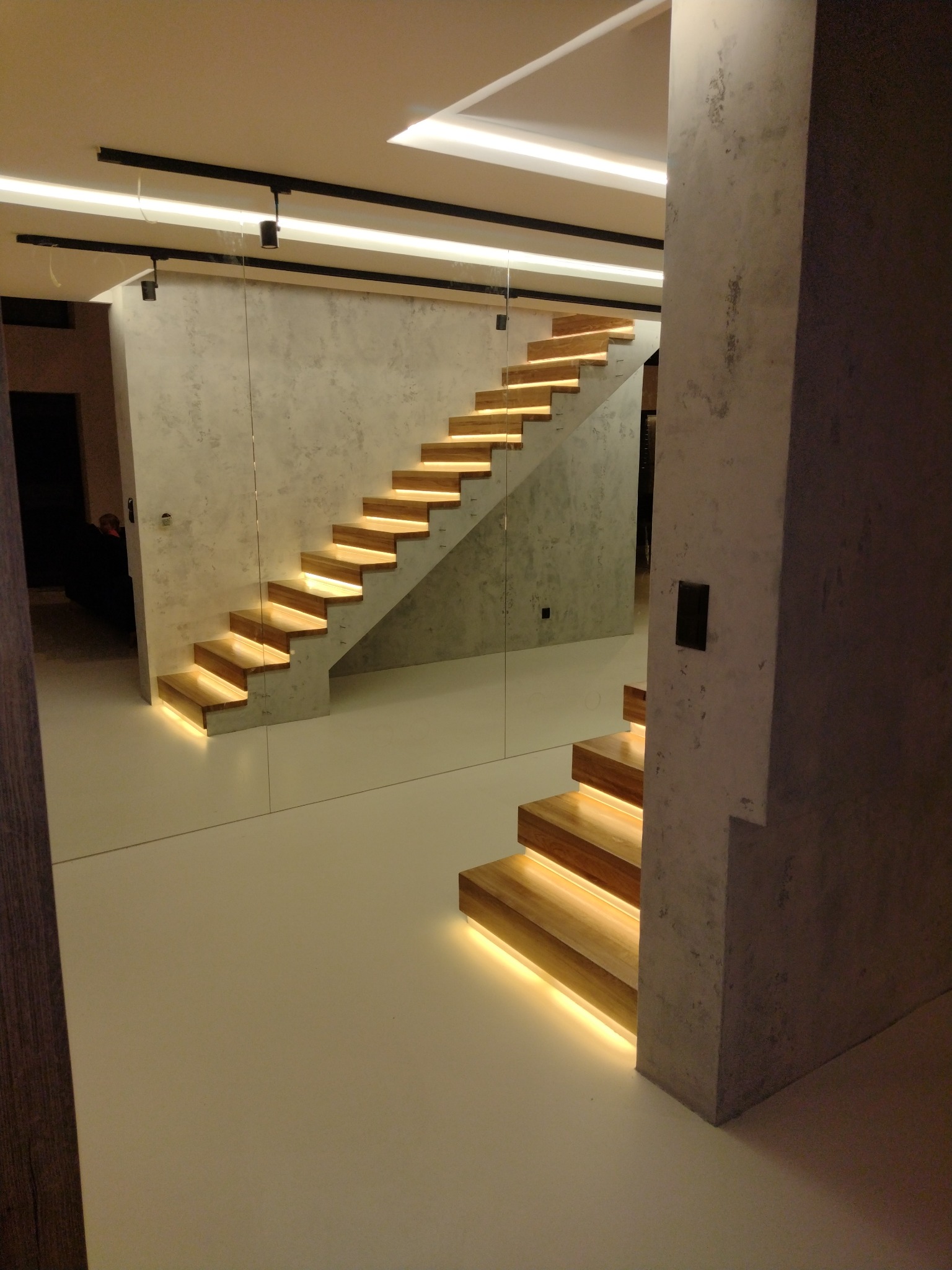 Nowoczesne schody drewniane z podświetleniem LED, wspornikowe, na tle ściany o fakturze betonu, widoczne w lustrzanym odbiciu.