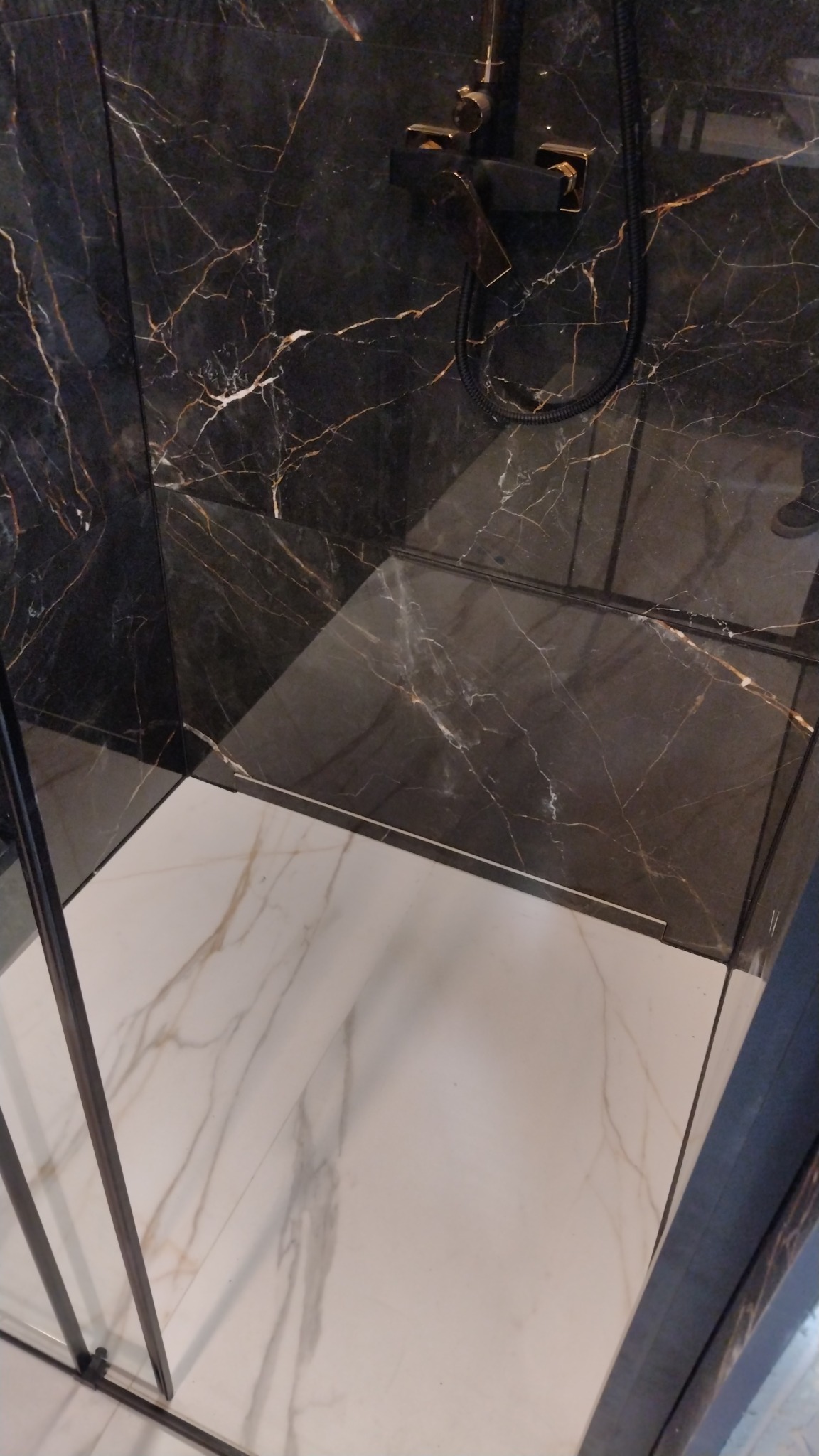Kabina prysznicowa z czarnymi marmurowymi ścianami z złotymi żyłami i białą marmurową podłogą, czarna armatura.