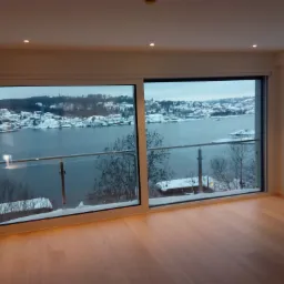 Jasne, puste wnętrze z dużymi oknami przesuwnymi, widok na zimowy krajobraz z jeziorem i zabudowaniami pokrytymi śniegiem, parkiet z jasnego drewna