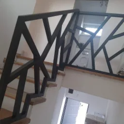 Nowoczesna balustrada schodowa z geometrycznym wzorem, czarna stal, widok na łazienkę i nieukończone wykończenie schodów.