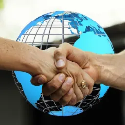 Uścisk dłoni na tle grafiki przedstawiającej globus, symbolizujący globalną współpracę.