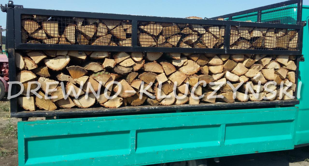 Załadunek pociętego, jasnego drewna w metalowej klatce na platformie turkusowej ciężarówki z napisem 'DREWNO-KLUCZYNSKI'.