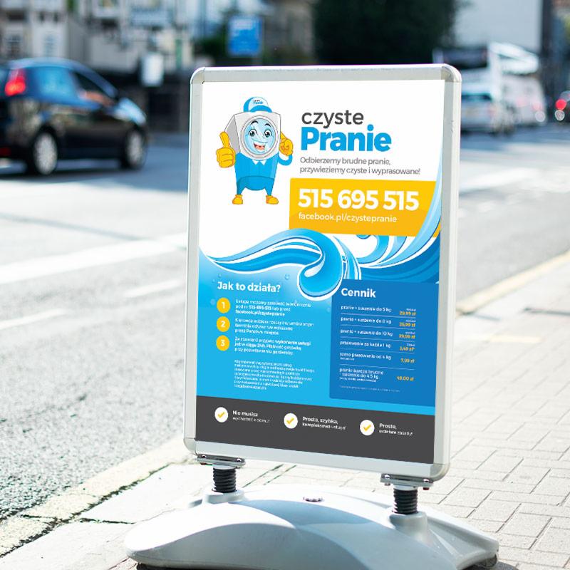 Reklamowy plakat wolnostojący na chodniku, promujący pralnię 'Czyste Pranie' z wesołą animowaną pralką, numerem telefonu i cennikiem usług.
