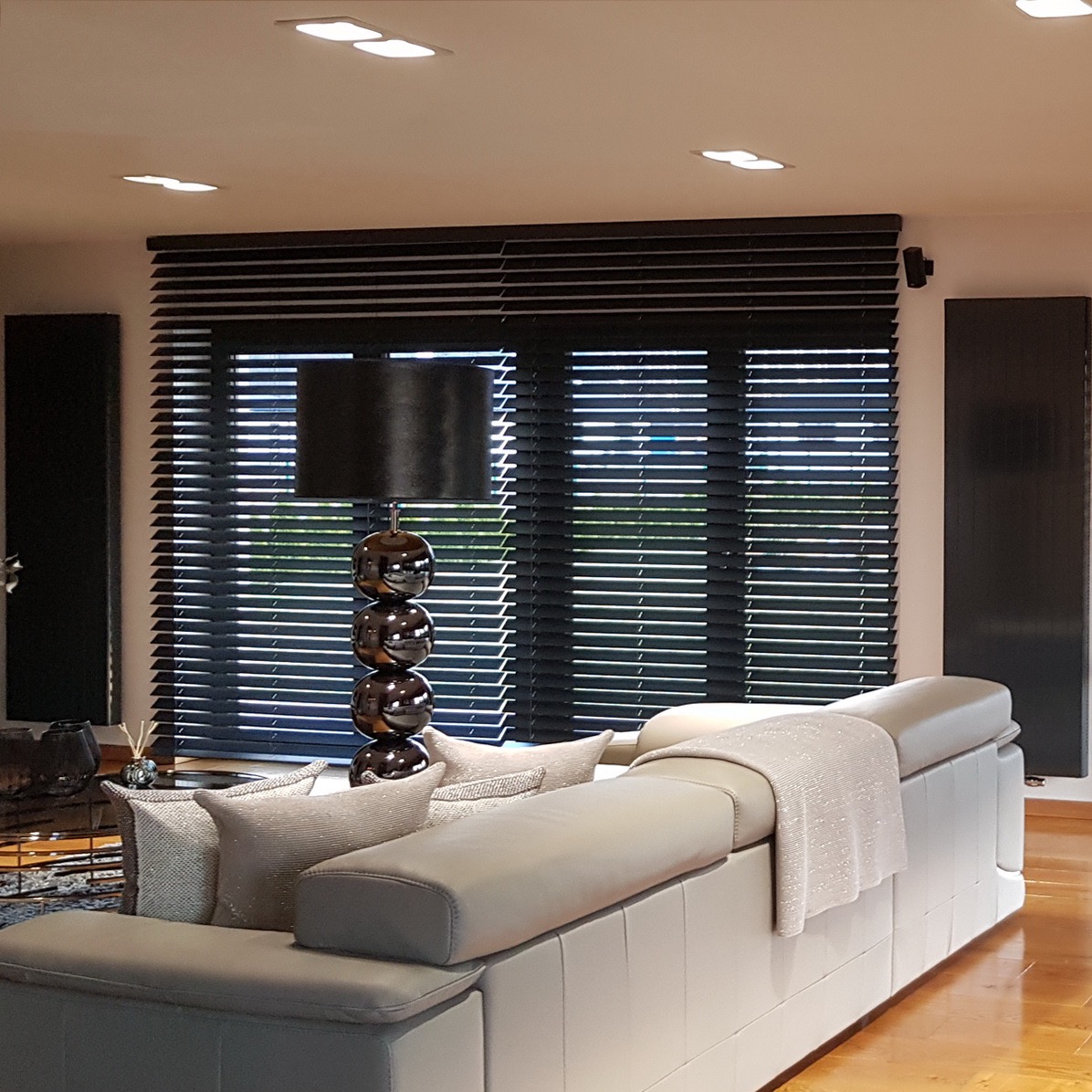 Salon z nowoczesnymi, czarnymi żaluzjami drewnianymi, szarym narożnikiem i lampą z kulistych elementów.