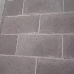 Szara ściana z bloczków betonowych połączonych zaprawą, widoczne spoiny i porowata struktura materiału.