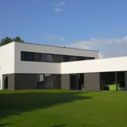 Nowoczesny dom z białą elewacją i szarym cokołem, duże okna, zadbany trawnik, błękitne niebo z delikatnymi chmurami w tle.