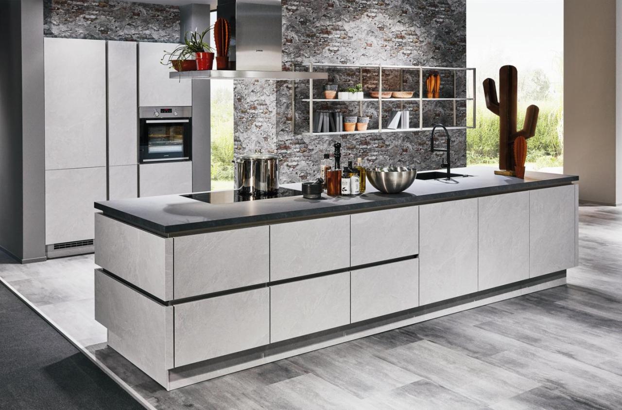 Nowoczesna kuchnia z szarymi frontami i blatem w odcieniach szarości, na wyspie kuchennej akcesoria kuchenne i dekoracyjny kaktus, ściana wykończona imitacją cegły.