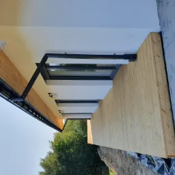 Elewacja domu z jasnego drewna z czarnymi rynnami i oknami, widok z dołu, w tle zieleń drzew