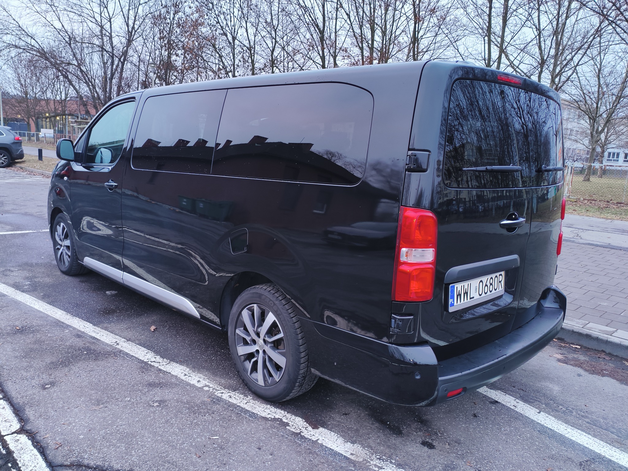Czarny bus marki Peugeot zaparkowany na parkingu, widok z tyłu i boku, tablica rejestracyjna WWL 0680R, jesienne drzewa w tle.