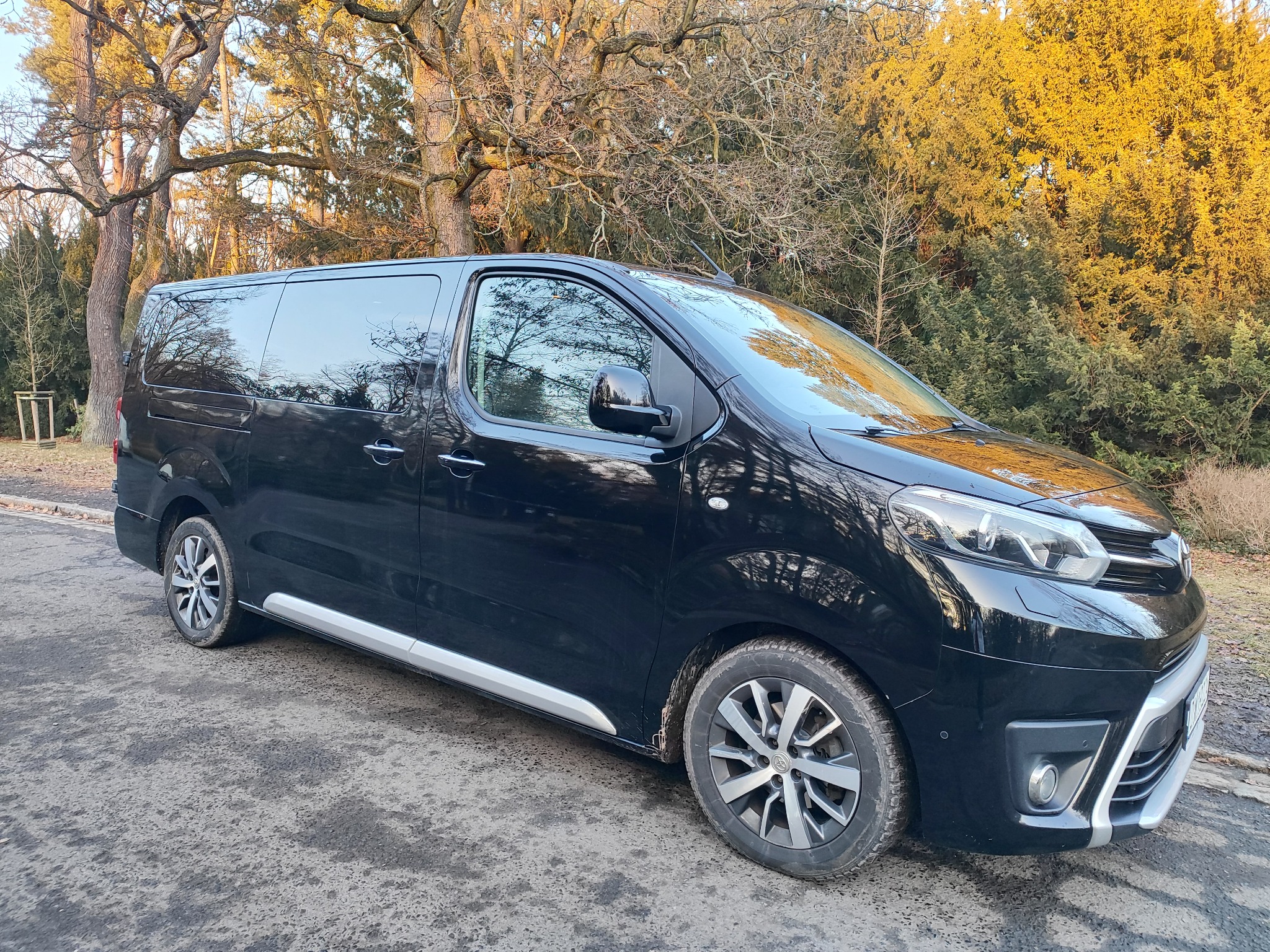 Czarny bus z przyciemnianymi szybami na tle drzew w jesiennej scenerii, Wrocław. Auto zaparkowane na uboczu, gotowe do transportu.