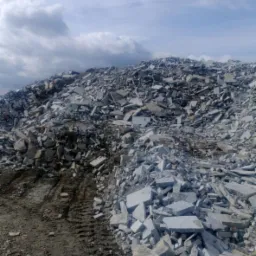 Góra potłuczonych płyt betonowych z widocznymi śladami opon na ziemi i pochmurnym niebem w tle.