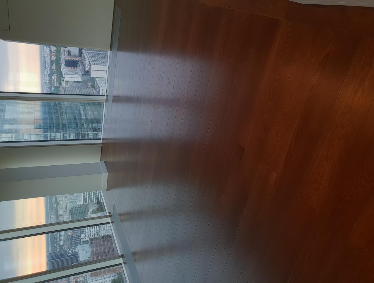 Świeżo ułożony, błyszczący parkiet z ciemnego drewna w apartamencie z widokiem na panoramę miasta o zachodzie słońca.