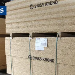 Stosy płyt budowlanych marki Swiss Krono, zabezpieczone taśmami, z widocznym logo producenta i etykietami informacyjnymi na paletach.