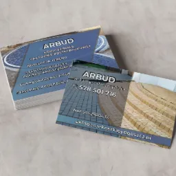 Dwie wizytówki firmy brukarskiej Arbud, z widocznymi danymi kontaktowymi i zdjęciami ułożonej kostki brukowej, leżące na szarej powierzchni.