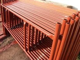 Rząd pomarańczowych, metalowych rusztowań budowlanych ułożonych jeden na drugim, widocznych pod kątem, z fragmentem ściany w tle.