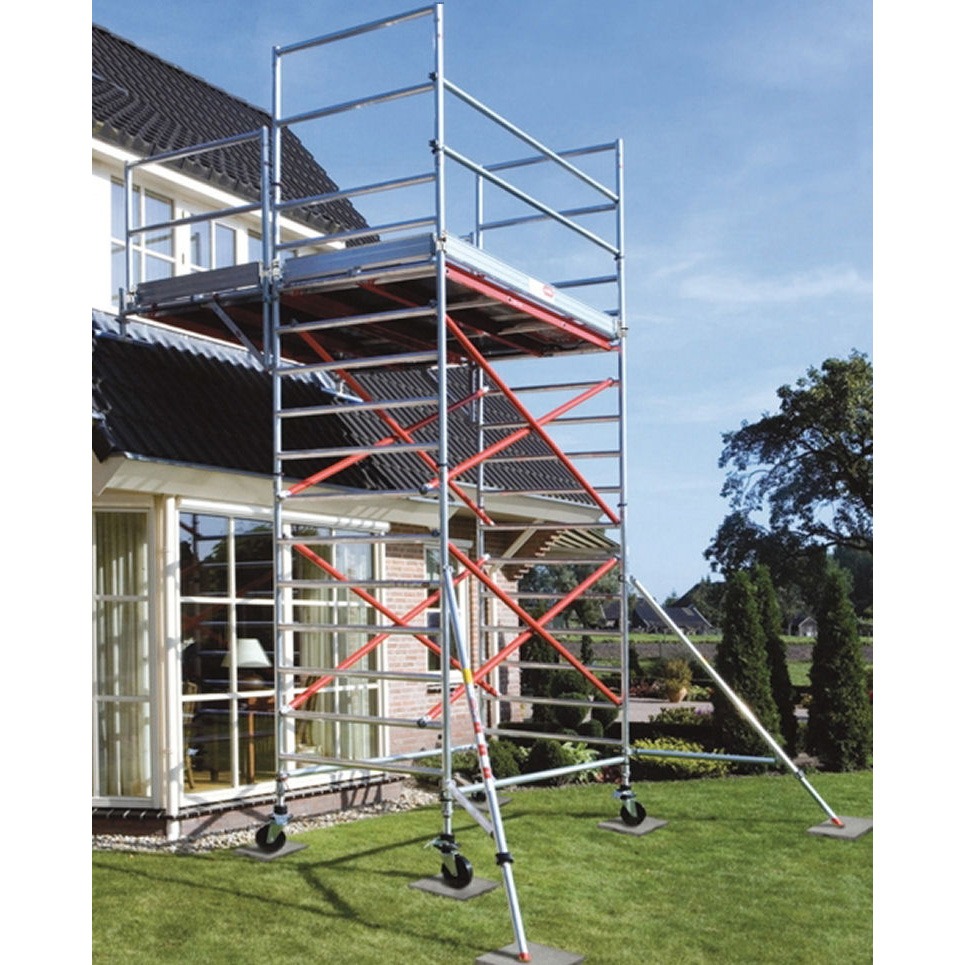 Aluminiowe rusztowanie na trawniku przed domem z cegły. Widoczne okna i dach. Konstrukcja z czerwonymi wzmocnieniami, na kółkach z regulowanymi podporami.