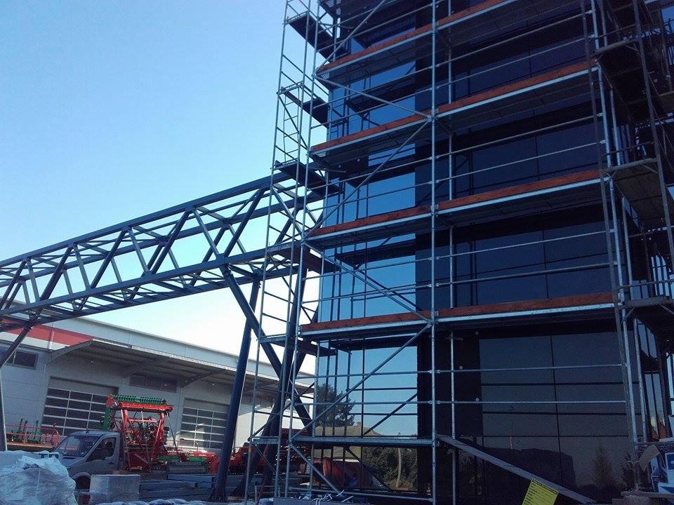 Montaż szklanej elewacji biurowca w Łodzi, widoczne rusztowania i metalowa konstrukcja łącząca budynki.