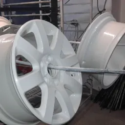 Białe felgi samochodowe po nałożeniu lakieru proszkowego, zawieszone na metalowych prętach w warsztacie.