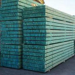 Sama - Stos impregnowanych na zielono desek drewnianych ułożonych w równe warstwy, widoczny fragment nieba w tle.