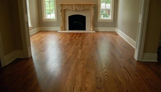 Błyszcząca, odnowiona drewniana podłoga w pustym pokoju z kominkiem i białymi listwami przypodłogowymi, widok z niskiego kąta.