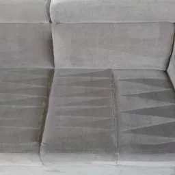 Szara, tapicerowana kanapa z widocznymi, jaśniejszymi śladami po czyszczeniu na siedzisku, ukazującymi wz&oacute;r w zygzaki.