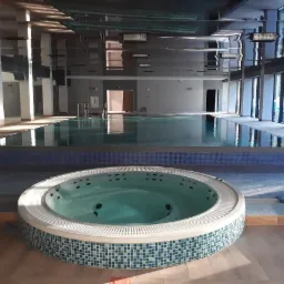 Wnętrze nowo wybudowanego basenu z jacuzzi, wykończone mozaiką w odcieniach błękitu i zieleni, z odbiciem światła w lustrzanym suficie.