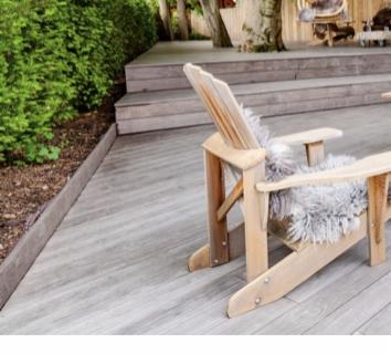 Drewniany taras z krzesłem Adirondack wyłożonym szarą skórą, schody prowadzące do podwyższonej części tarasu z widocznym pniem drzewa w tle.