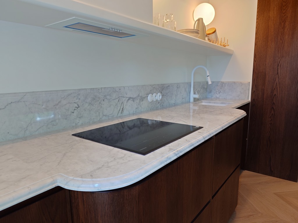 Elegancki blat kuchenny z marmuru z wbudowaną płytą indukcyjną. Zaokrąglone krawędzie blatu harmonizują z nowoczesnym designem kuchni.