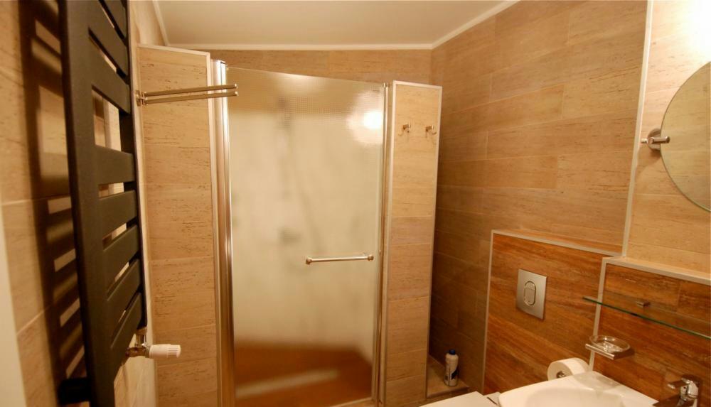 Wykończona łazienka z kabiną prysznicową z matowego szkła, grzejnikiem drabinkowym w kolorze grafitowym, płytkami imitującymi drewno na ścianach i okrągłym lustrem.