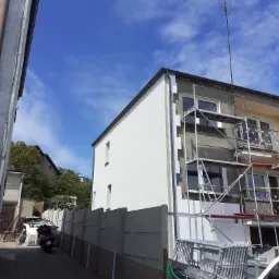 Budynek w trakcie prac elewacyjnych: fragment ocieplony styropianem, część z nałożonym tynkiem, rusztowanie, widoczny numer domu 11 na sąsiednim budynku.