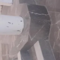 Szare marmurowe płytki ułożone wokół rury w rogu pomieszczenia, widoczne białe żyłki w kamieniu.