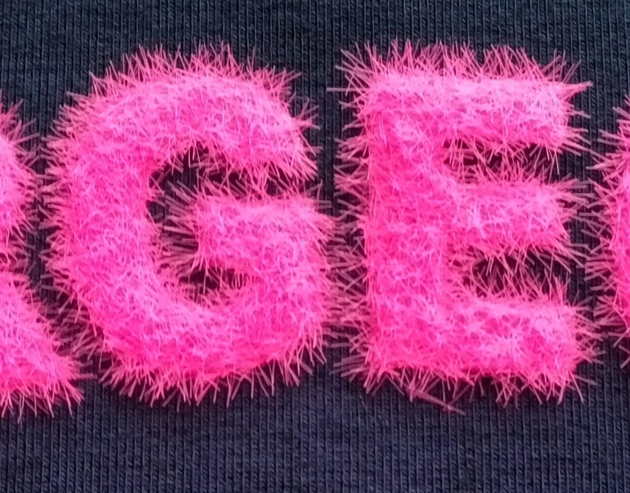 Fragment czarnej koszulki z włochatym, różowym napisem w zbliżeniu.