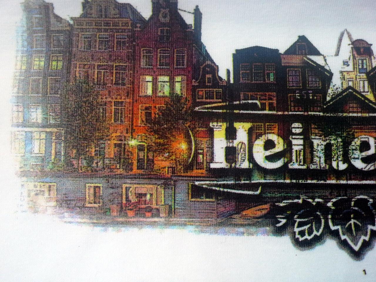 Koszulka z nadrukiem przedstawiającym kamienice w Amsterdamie z odbiciem w wodzie i napisem 'Heine' wkomponowanym w architekturę.