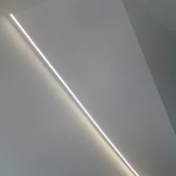 Minimalistyczne oświetlenie LED wpuszczone w gładką, białą ścianę pod kątem, tworzące subtelny efekt wizualny w rogu pomieszczenia.