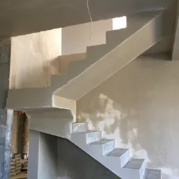 Surowe schody w trakcie wykańczania we Wrocławiu, z widocznymi workami materiałów budowlanych w tle i niedoskonałościami na ścianie.