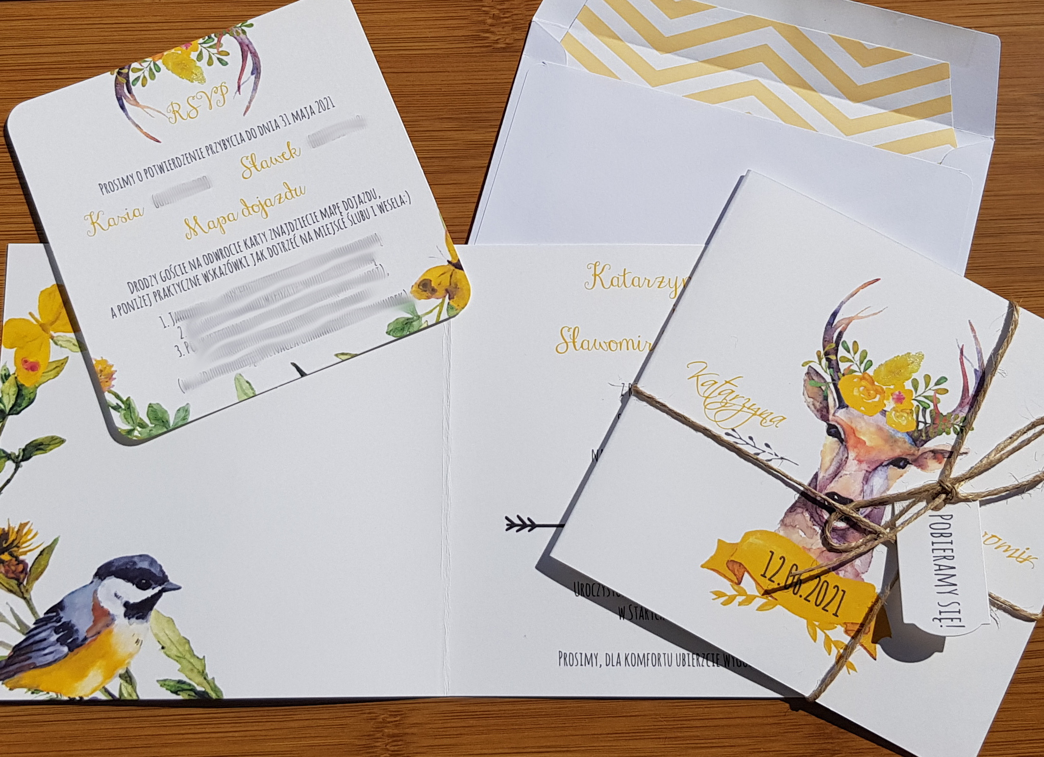 Komplet zaproszeń ślubnych z motywem jelenia i kwiatów, z kopertą w złote zygzaki, leżących na drewnianym stole.