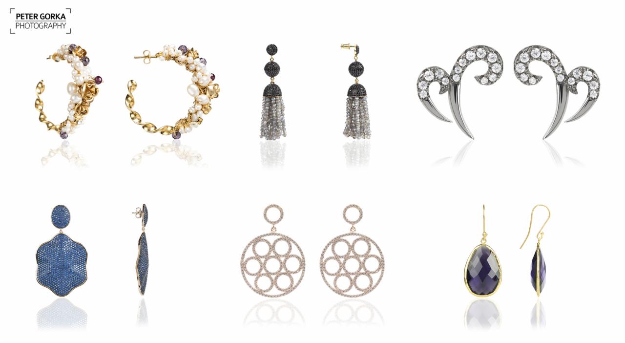 Kolekcja różnorodnych kolczyków na białym tle: koła z perłami, czarne kule z frędzlami, srebrne spirale z cyrkoniami, niebieskie kwiaty z kamieni i fioletowe łezki w złotej oprawie.