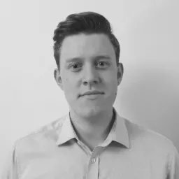 Portret młodego mężczyzny w koszuli, z krótką fryzurą, na jasnym tle. Zdjęcie w czerni i bieli, z delikatnym oświetleniem.