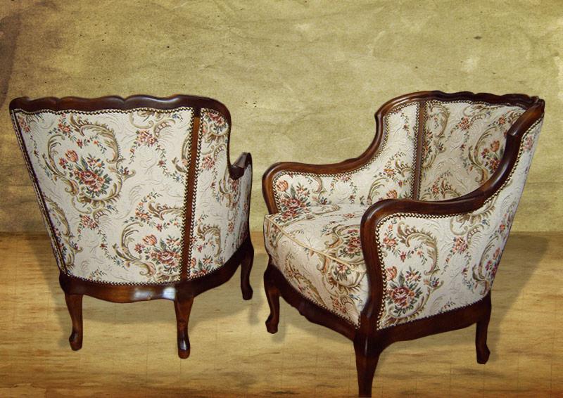 Dwa klasyczne fotele tapicerowane tkaniną w kwiaty, z ciemnobrązowymi drewnianymi ramami, ustawione na tle teksturowanej ściany.