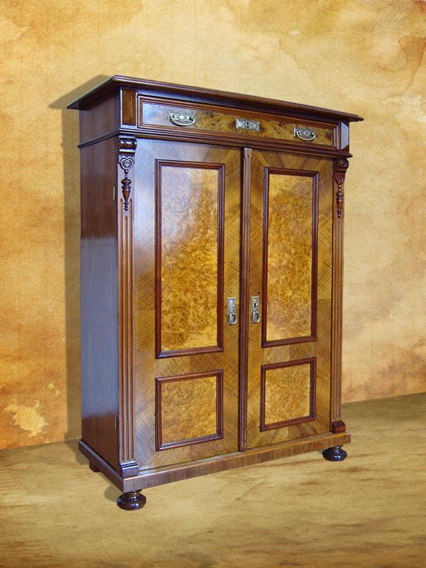 Odrestaurowana, dwudrzwiowa szafa z fornirem o wzorze ptasiego oka, z dekoracyjnymi kolumnami i szufladą na górze, stojąca na ciemnych, kulistych nóżkach.
