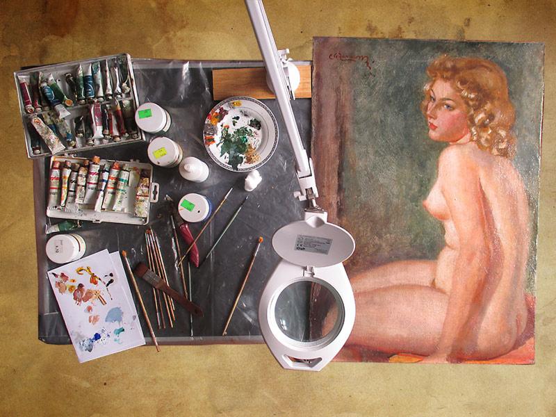 Warsztat malarski: obraz olejny aktu kobiecego, farby w tubkach i pudełkach, pędzle różnych rozmiarów, paleta z farbami i lampa powiększająca na stole.