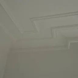 Biały sufit z dekoracyjnymi listwami i geometrycznym wzorem w rogu pomieszczenia, świeżo po malowaniu.