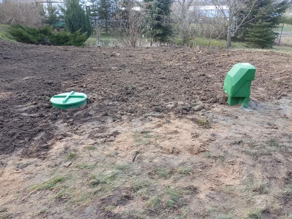 Zielona pokrywa włazu i odpowietrznik na świeżo przekopanej ziemi, prawdopodobnie po instalacji systemu odprowadzania wody.