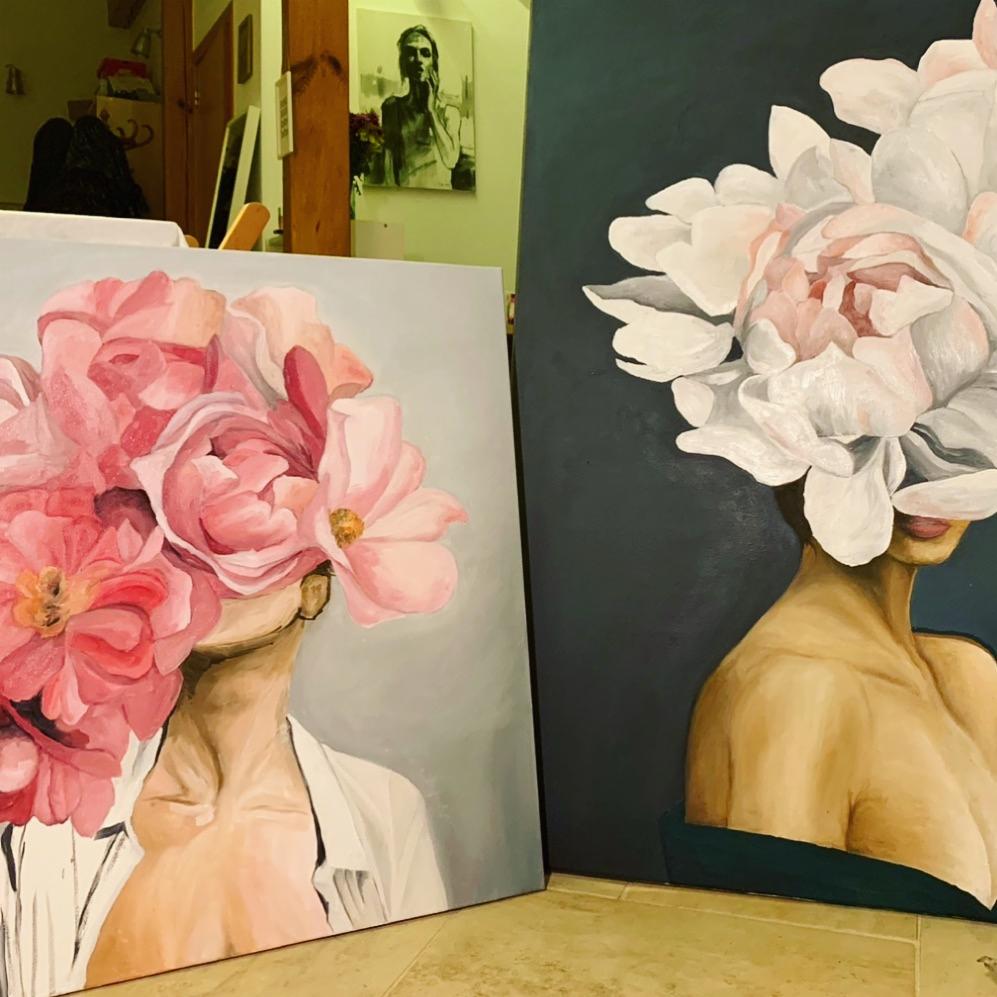 Dwa płótna z malowidłami przedstawiającymi kobiety, których twarze zastąpione są kwiatami: po lewej różowe magnolie, po prawej białe piwonie na ciemnym tle. Widoczny fragment ram i podłogi.